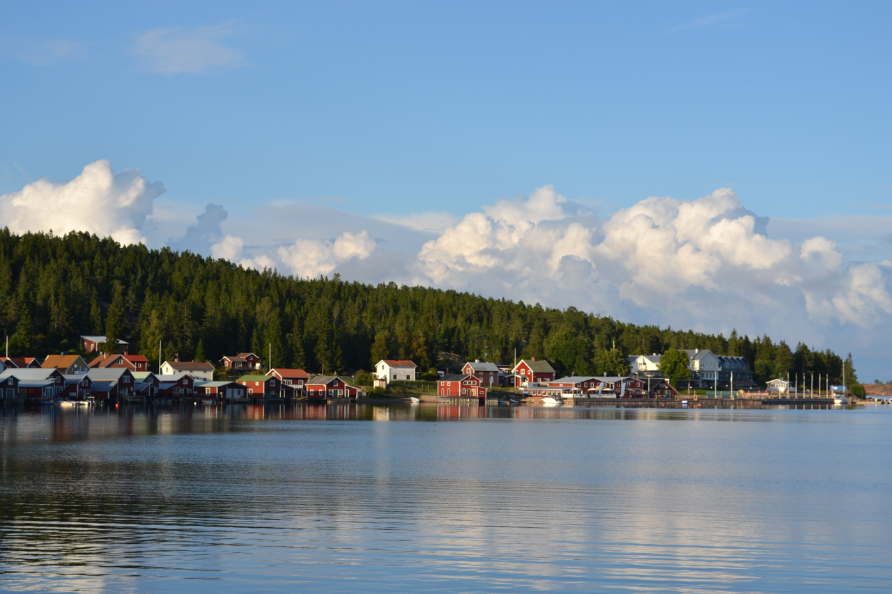 Ulvöhamn med sjöbodar och skog som speglar sig i stilla vatten
