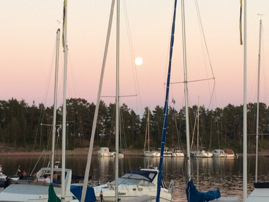 Segelbåtar i hamnen i skymningen med fullmånen över skogen