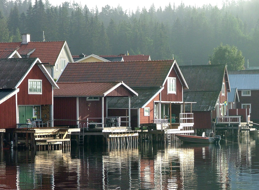 Röda sjöbodar som speglar sig i vattnet en dimmig morgon